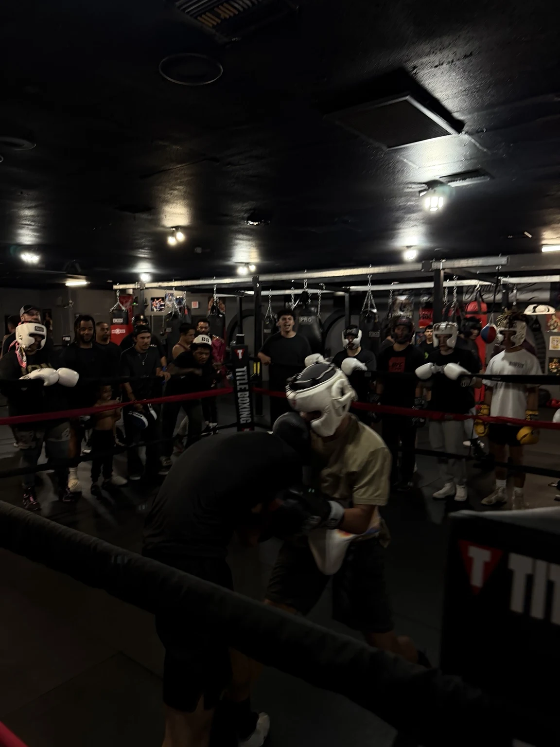 Two boxers sparring in the Fight Cartel ring while the gym community watches from the ropes